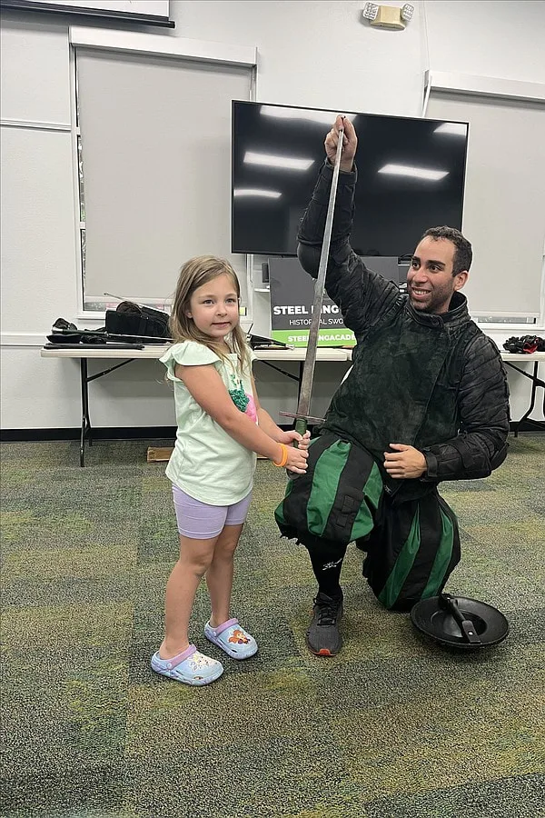 Instructor Chris at a summer reading program demonstration taking a photo with a child